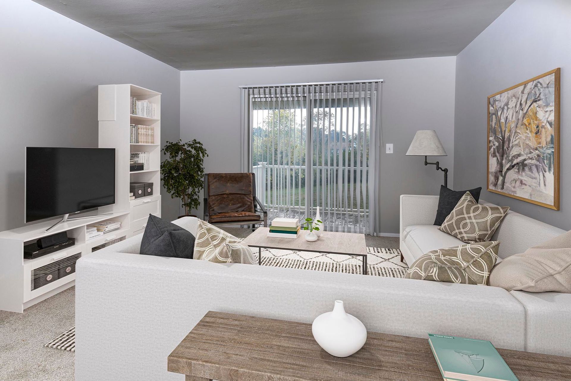 Living room in an apartment with white sofas, a TV stand, a bookshelf, and sliding glass door with vertical blinds at Chesapeake Pointe, offers apartments in Chesapeake, VA.