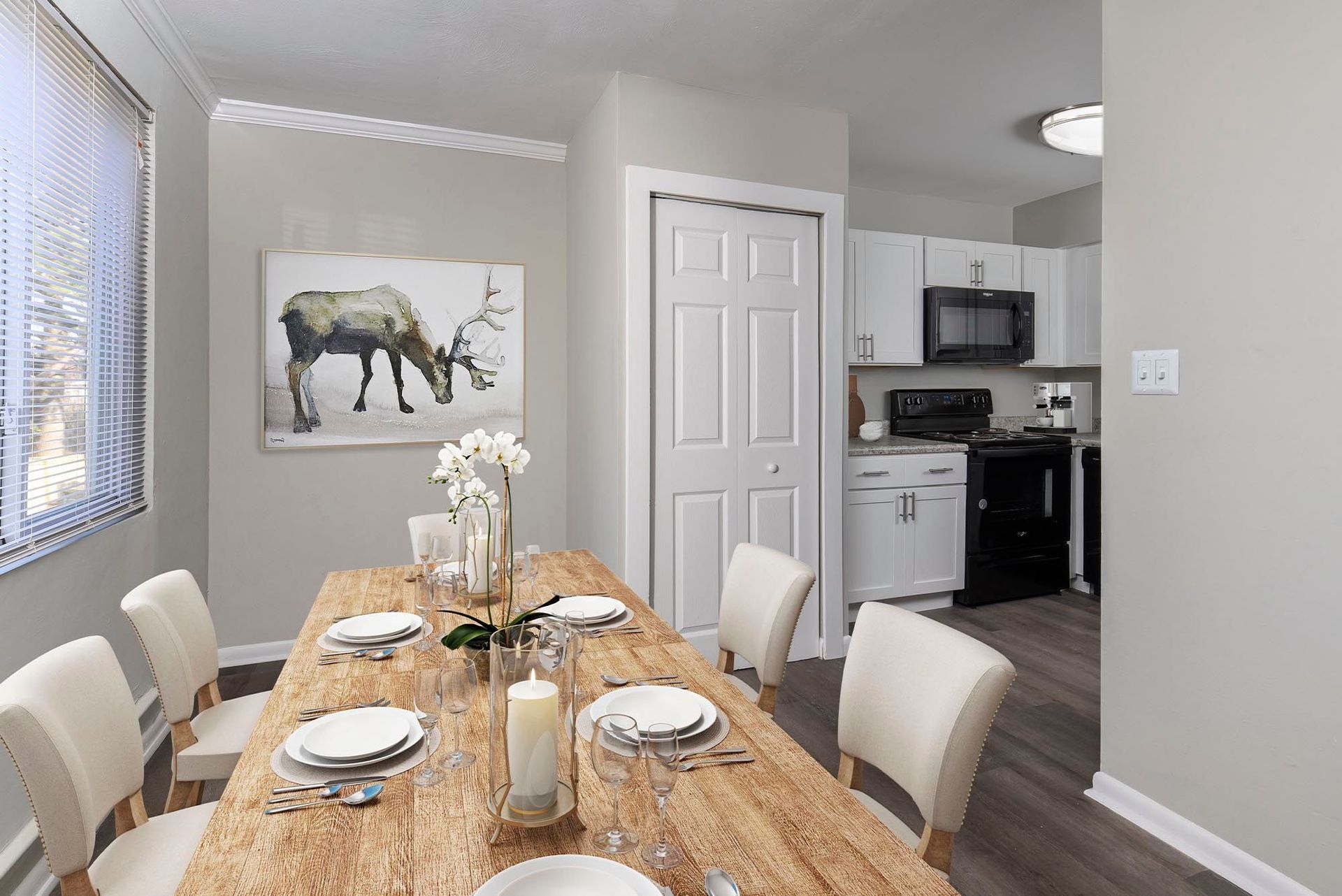 Dining area in an apartment with a wooden table, white chairs, and a kitchen in the background at Chesapeake Pointe, offers apartments in Chesapeake, VA.