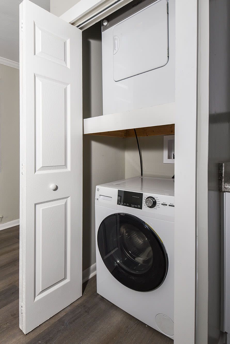 Stacked front-loading washer and dryer in an in-unit laundry closet with a shelf at Chesapeake Pointe, offers Apartments for Rent in Chesapeake, VA.