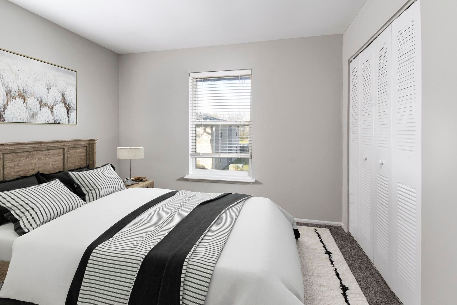 Bedroom in a modern apartment with gray walls, a wooden headboard, striped bedding, and a window at Chesapeake Pointe, offers Apartments for Rent in Chesapeake, VA.