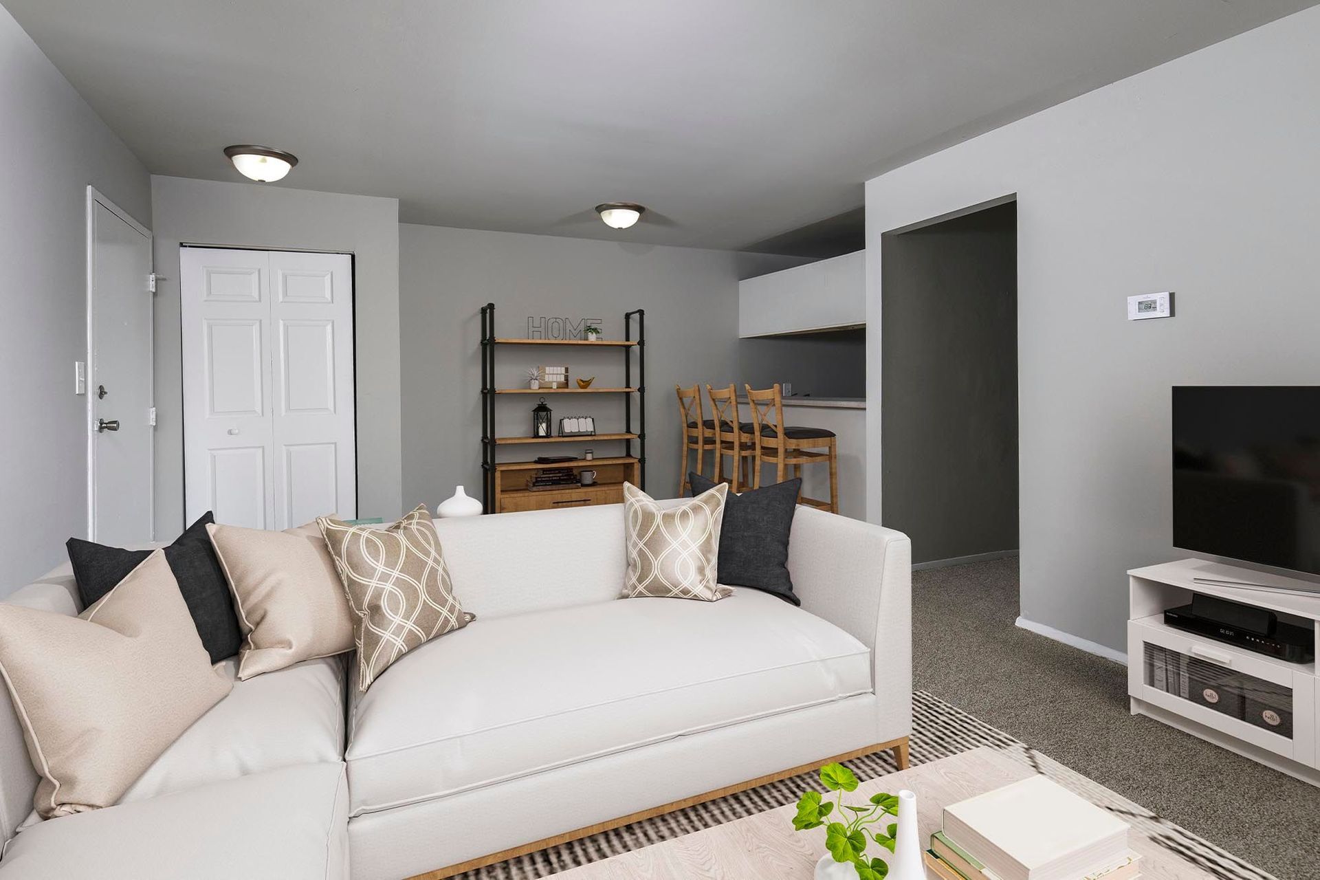 Basement-style apartment living room with white sectional sofa, TV, bar counter with stools, and open shelving  at Chesapeake Pointe, offers Chesapeake, VA apartments for rent.