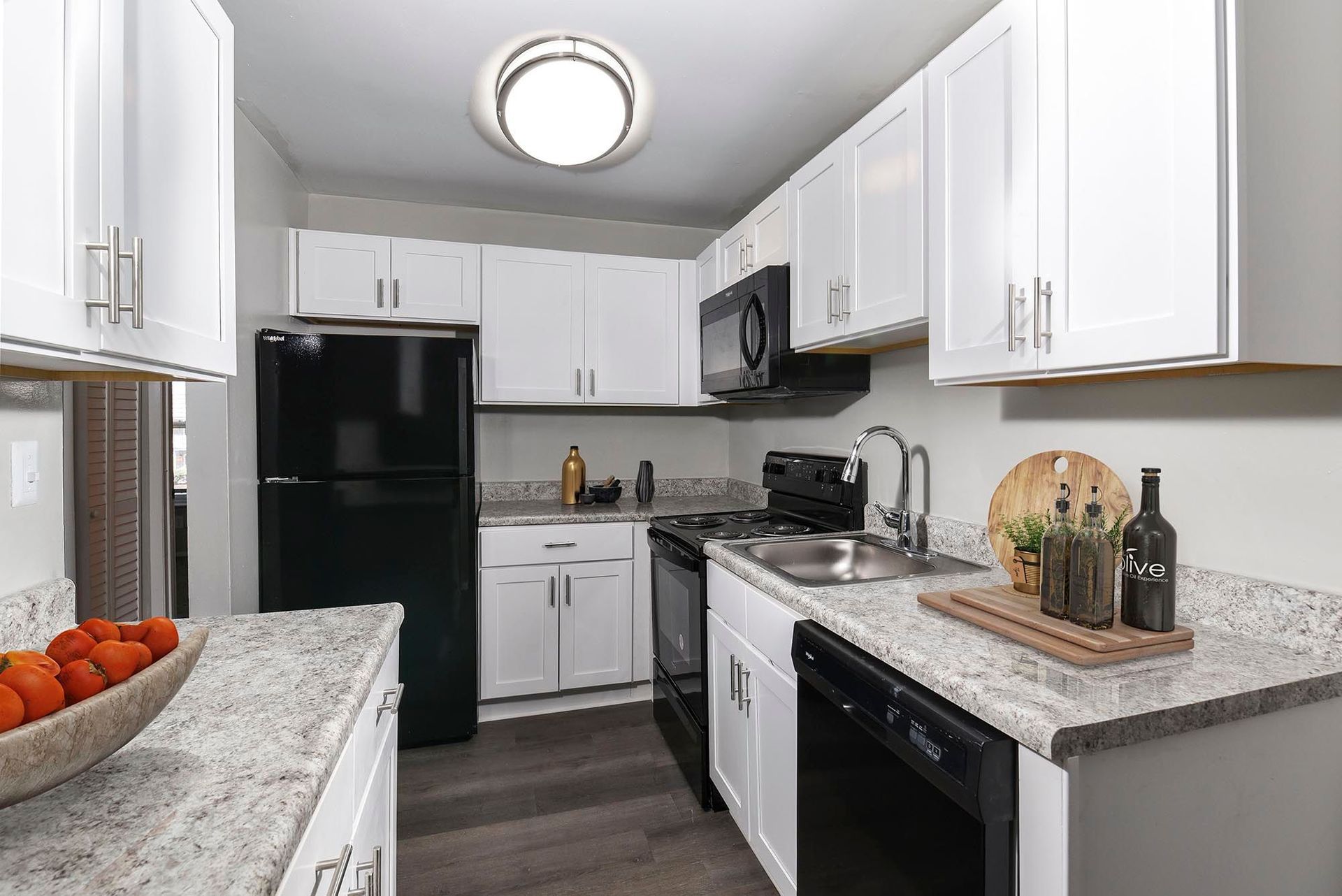 Bright white apartment kitchen with granite countertops, white cabinets, stainless sink, and black appliances at Chesapeake Pointe, offers Apartments for Rent in Chesapeake, VA.