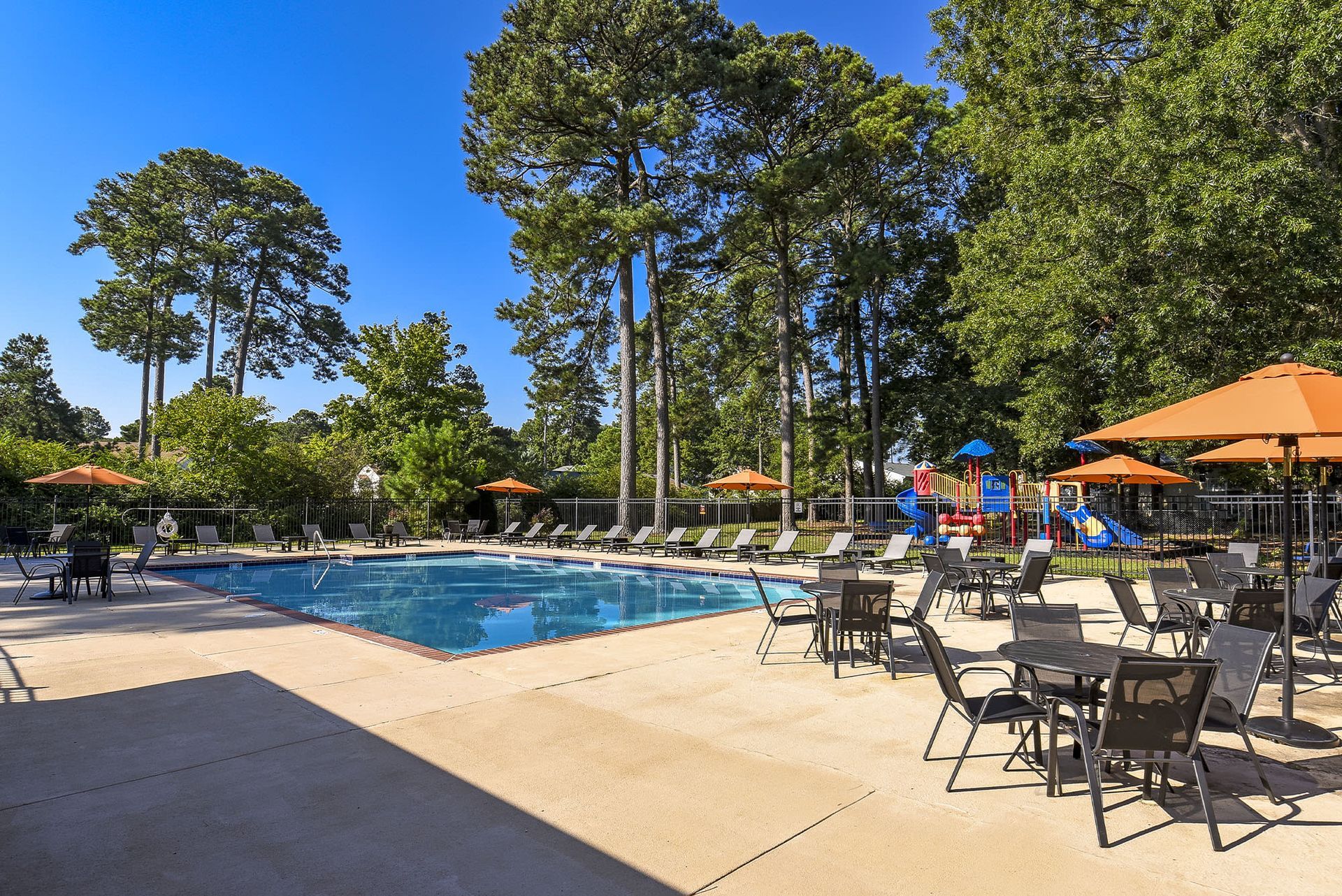 Outdoor community pool with lounge chairs, umbrellas, and tall trees at Chesapeake Pointe, offers  pet-friendly apartments in Chesapeake, VA