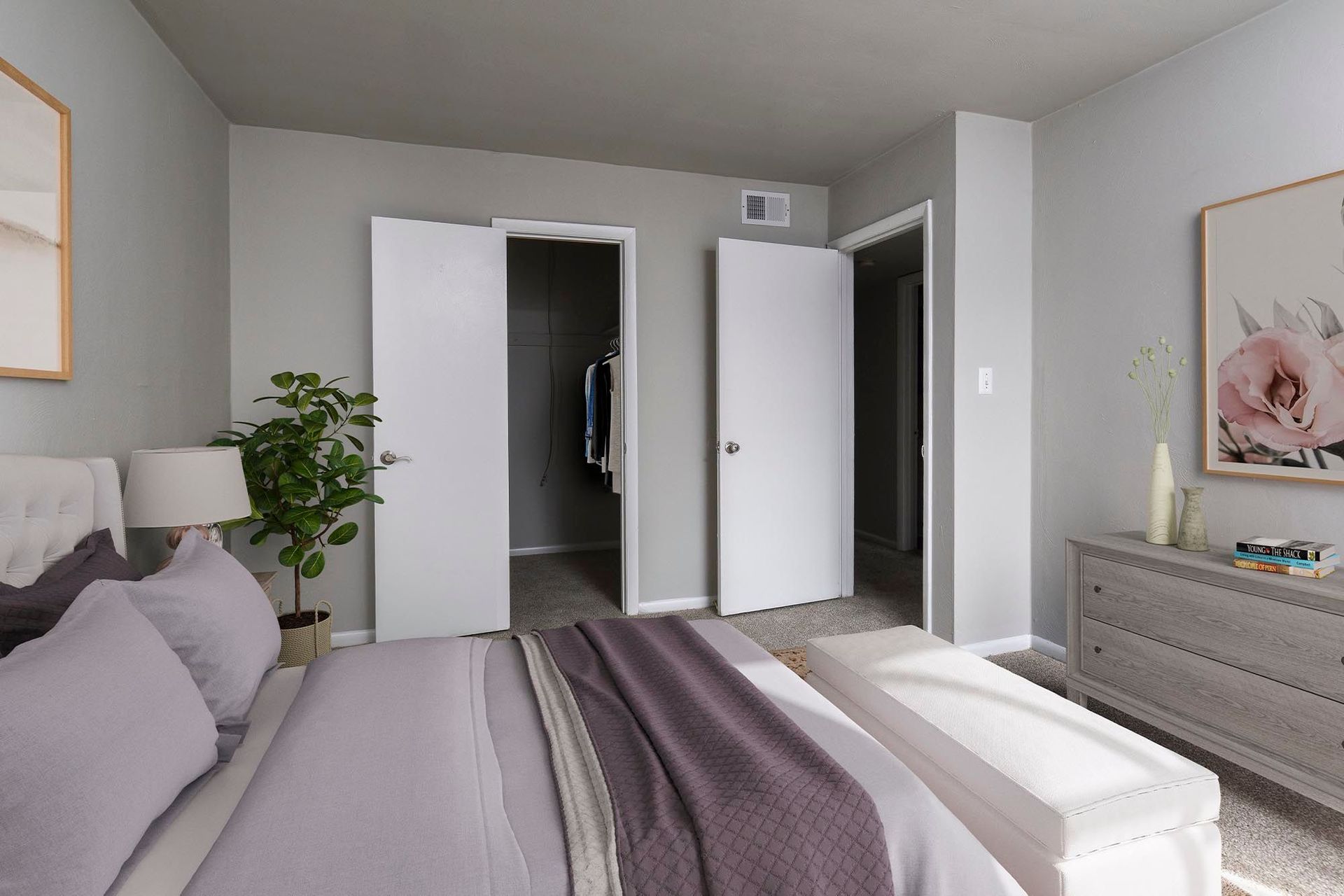Bedroom with gray walls, open closet doors, bed, plant, and dresser at Chesapeake Pointe, offers Chesapeake, VA apartments for rent.