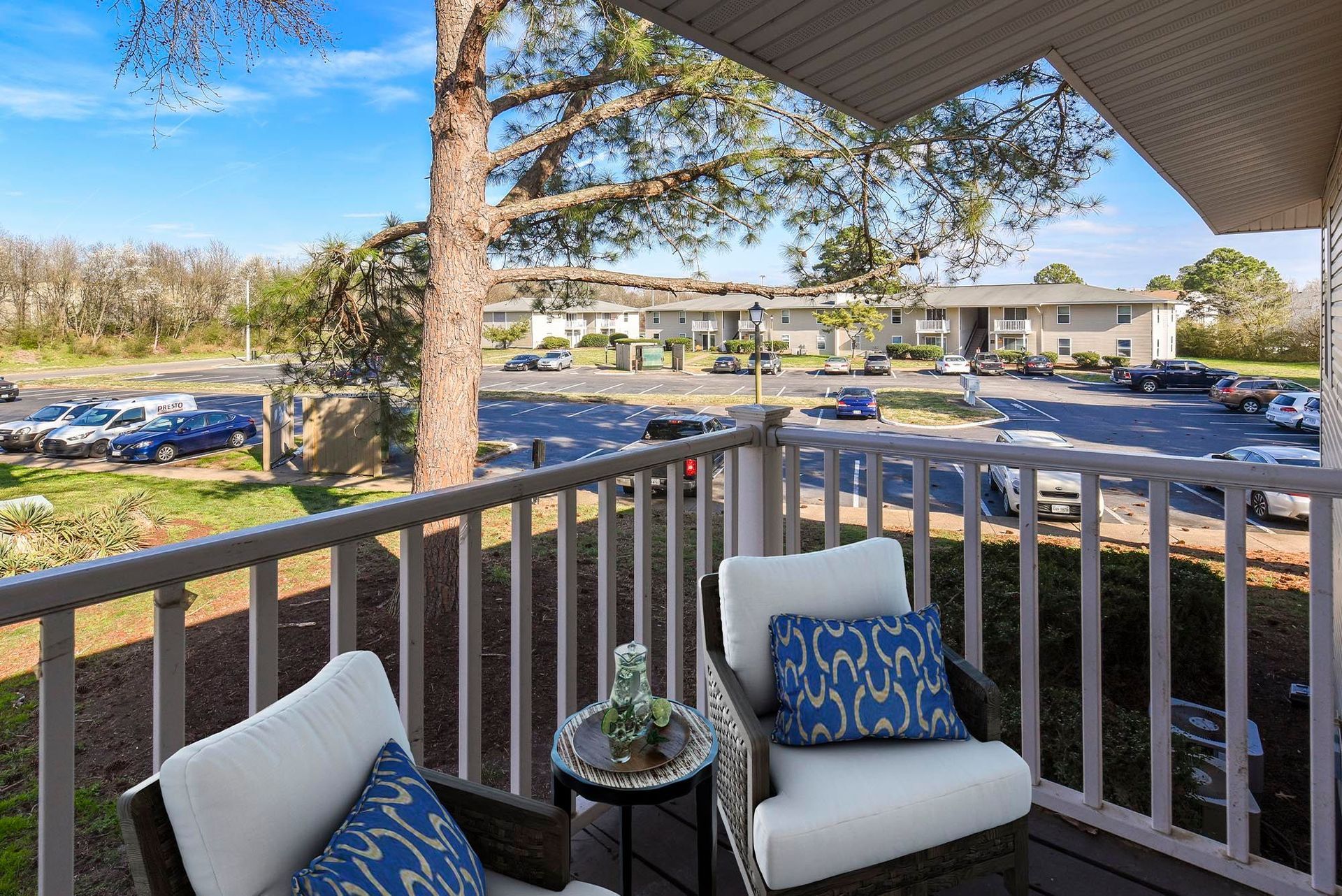Balcony with white cushioned chairs and blue pillows overlooking a parking lot at Chesapeake Pointe, offers apartments in Chesapeake, VA.