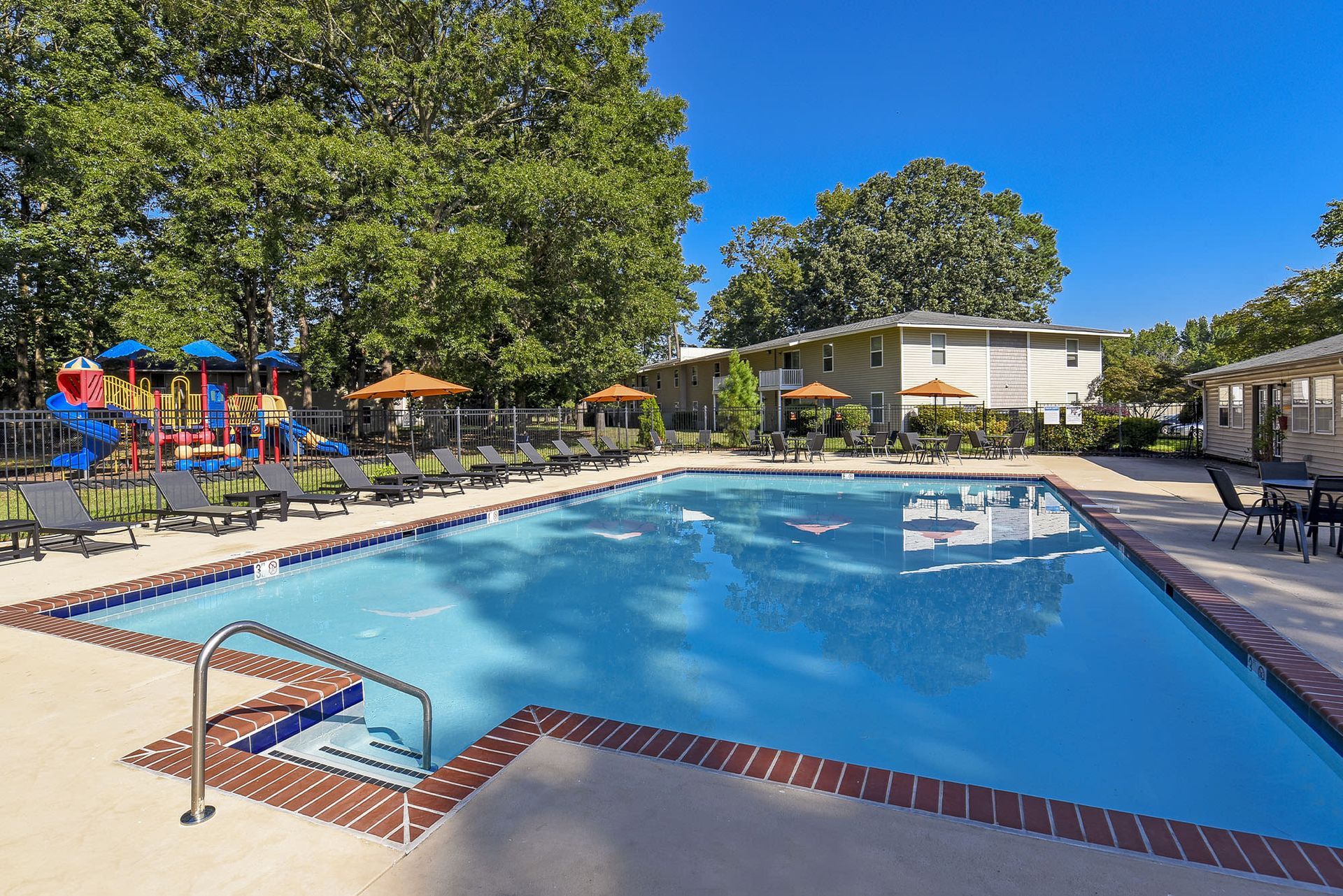 Outdoor community pool with lounge chairs, umbrellas, and a nearby playground at Chesapeake Pointe, offers  pet-friendly apartments in Chesapeake, VA