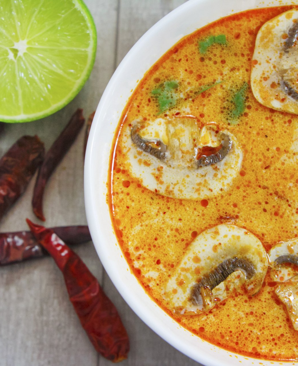 A bowl of soup with mushrooms and a slice of lime