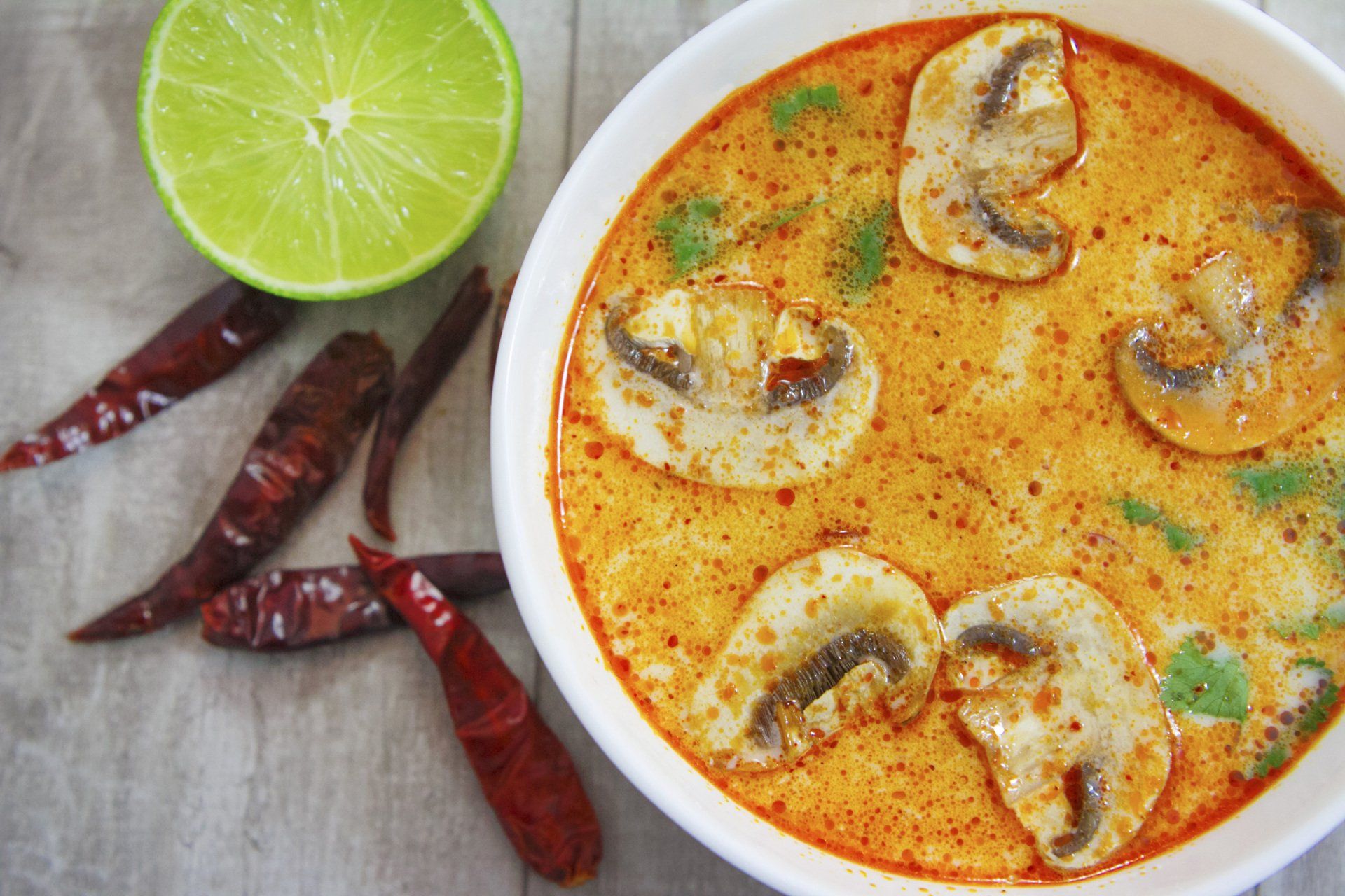 A bowl of soup with mushrooms and a lime on a table.
