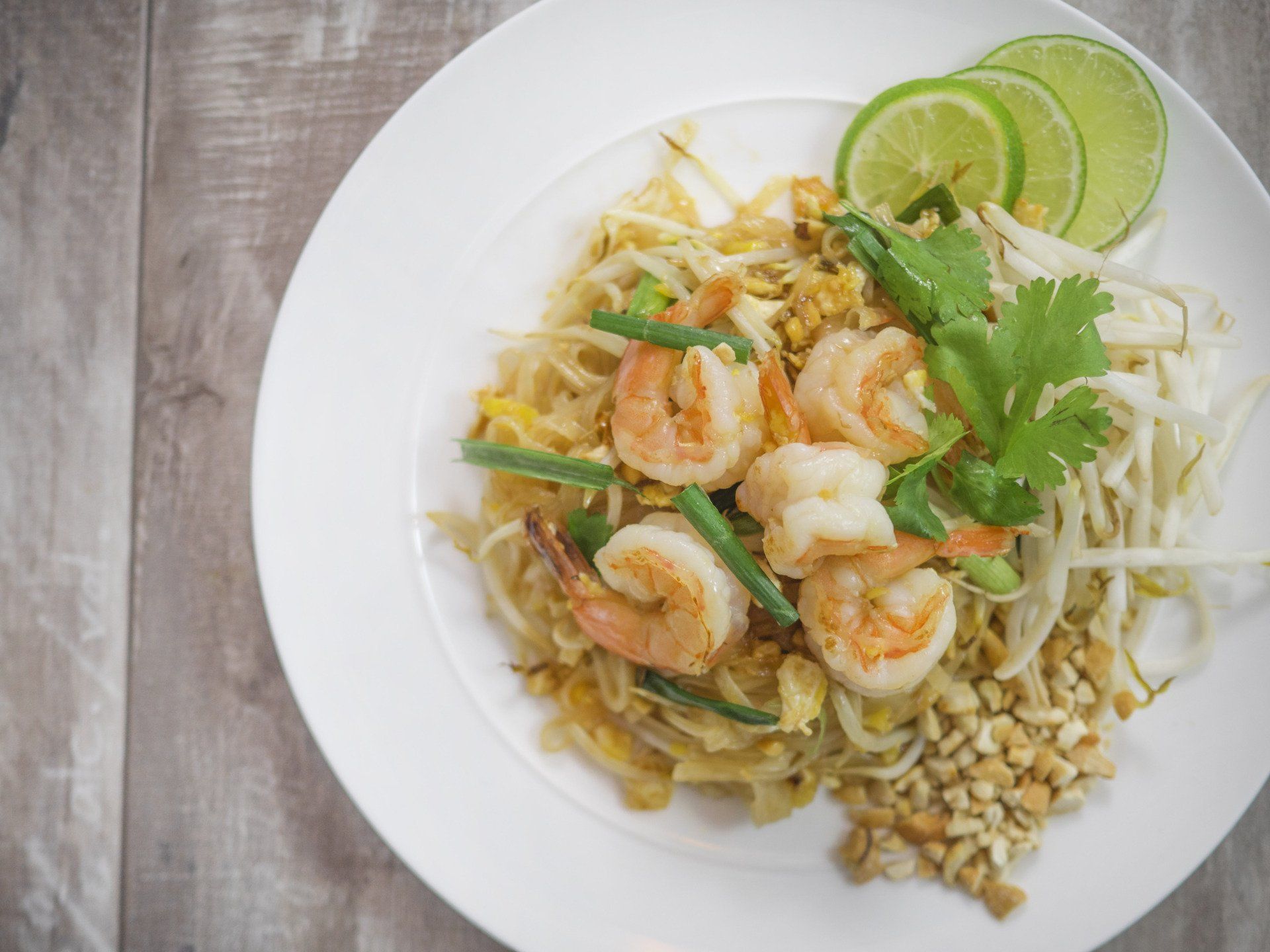 A white plate topped with shrimp and noodles on a wooden table.