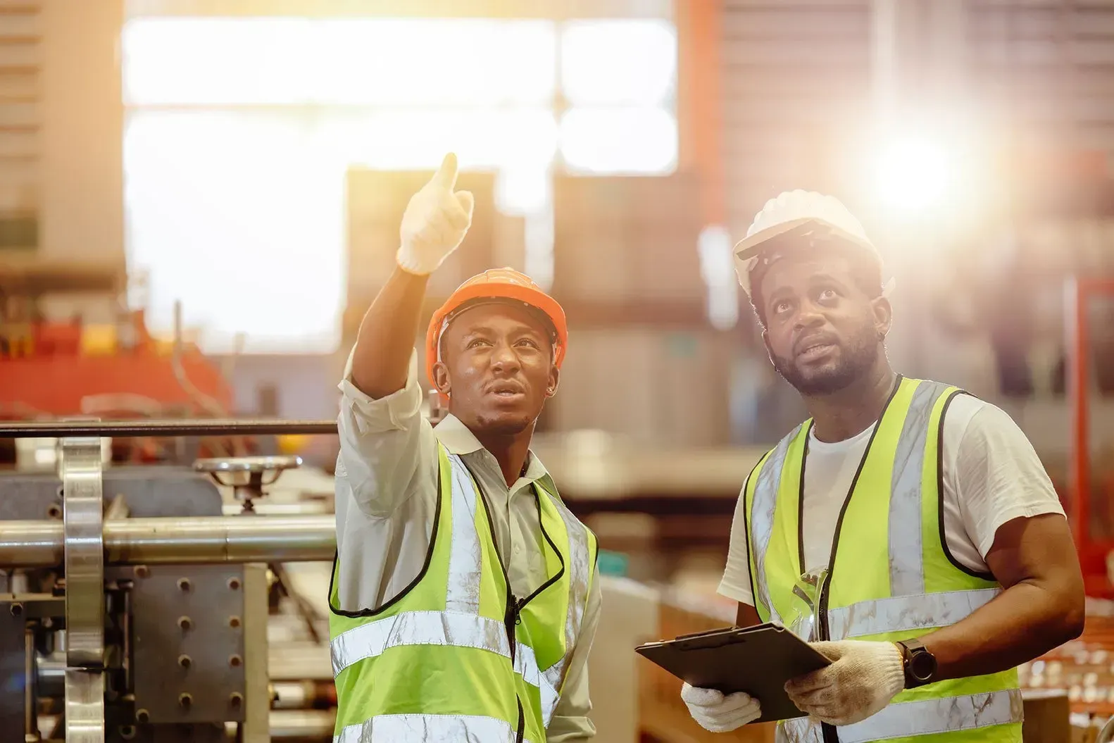 Deux hommes noirs portant des casques et des gilets de sécurité dans une usine.
