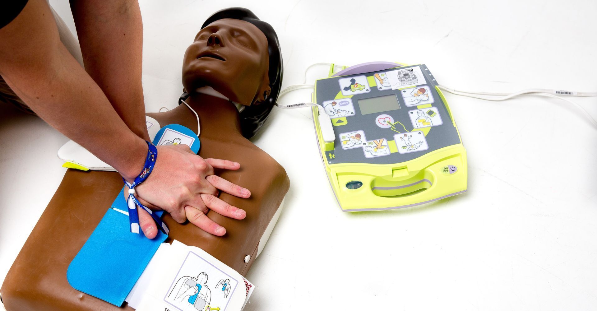 Une personne effectuant une réanimation cardio-pulmonaire sur un mannequin d'entraînement à côté d'un dispositif DEA.