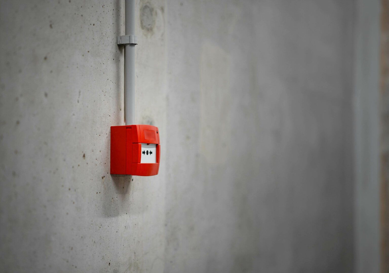 Alarme incendie rouge sur un mur en béton avec un conduit au-dessus.