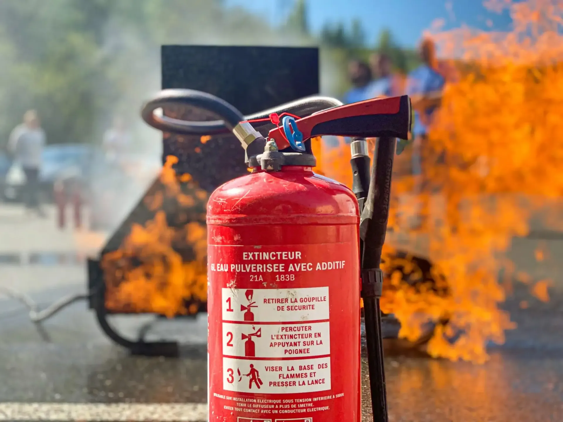 Extincteur rouge devant une structure en feu, à l'extérieur.