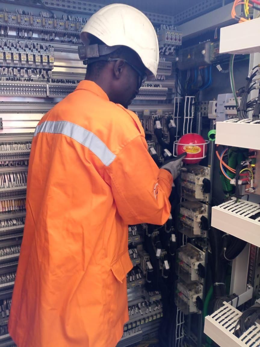 Ouvrier en combinaison orange et casque de sécurité travaillant à l'intérieur d'un panneau de contrôle.