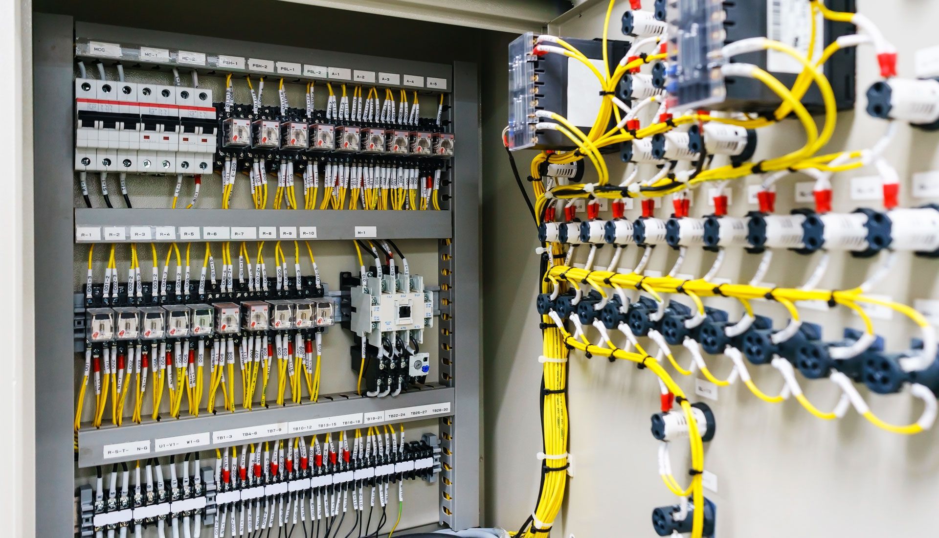 Panneau de contrôle électrique avec fils, bornes et disjoncteurs, câbles jaunes et blancs.