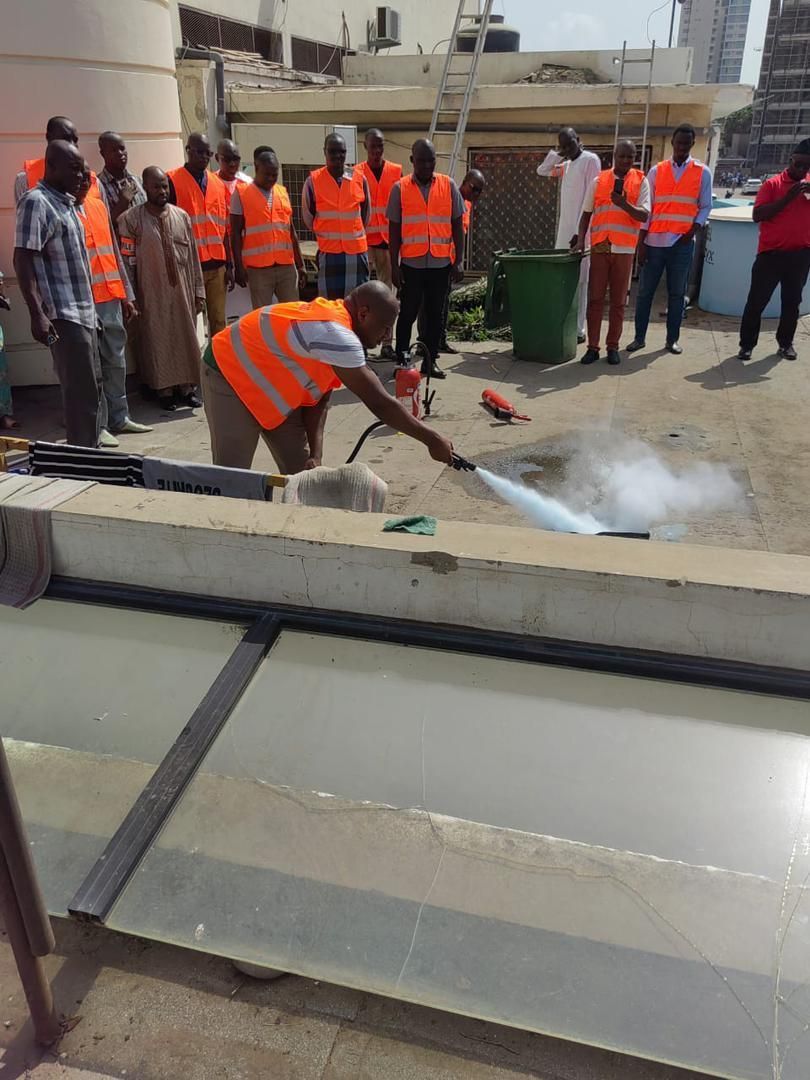 Groupe de personnes portant des gilets orange sur un toit ; l'une d'elles utilise un extincteur, créant un nuage.