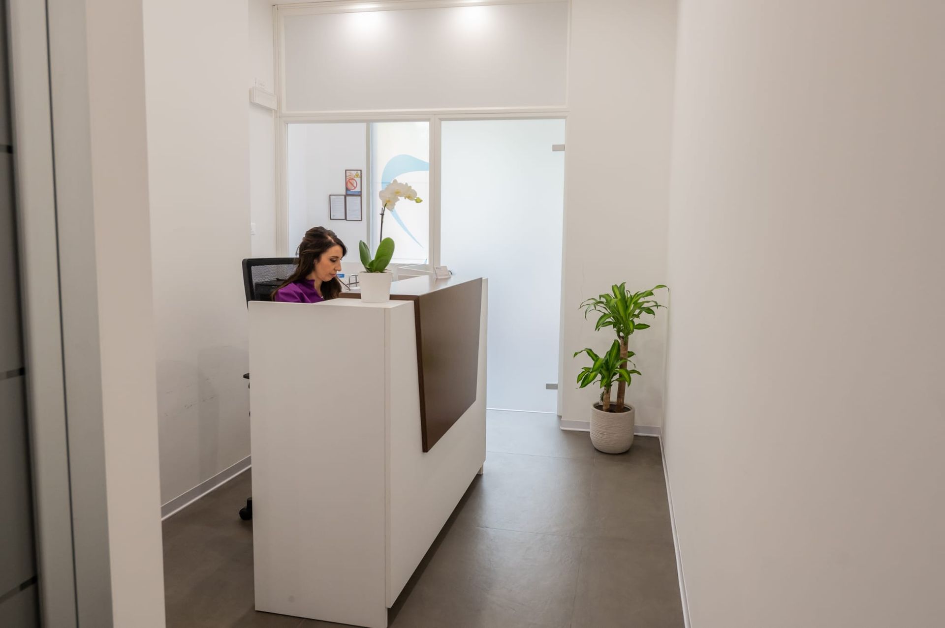 Una persona seduta a una moderna reception bianca in un ufficio ben illuminato, con una pianta in vaso nelle vicinanze.
