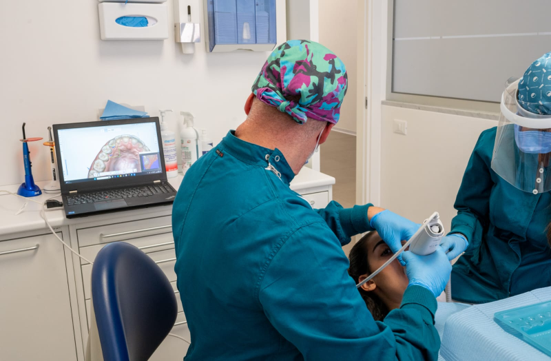 Un dentista utilizza uno scanner intraorale su un paziente, con il modello dentale 3D visualizzato sullo schermo di un computer portatile nelle vicinanze.