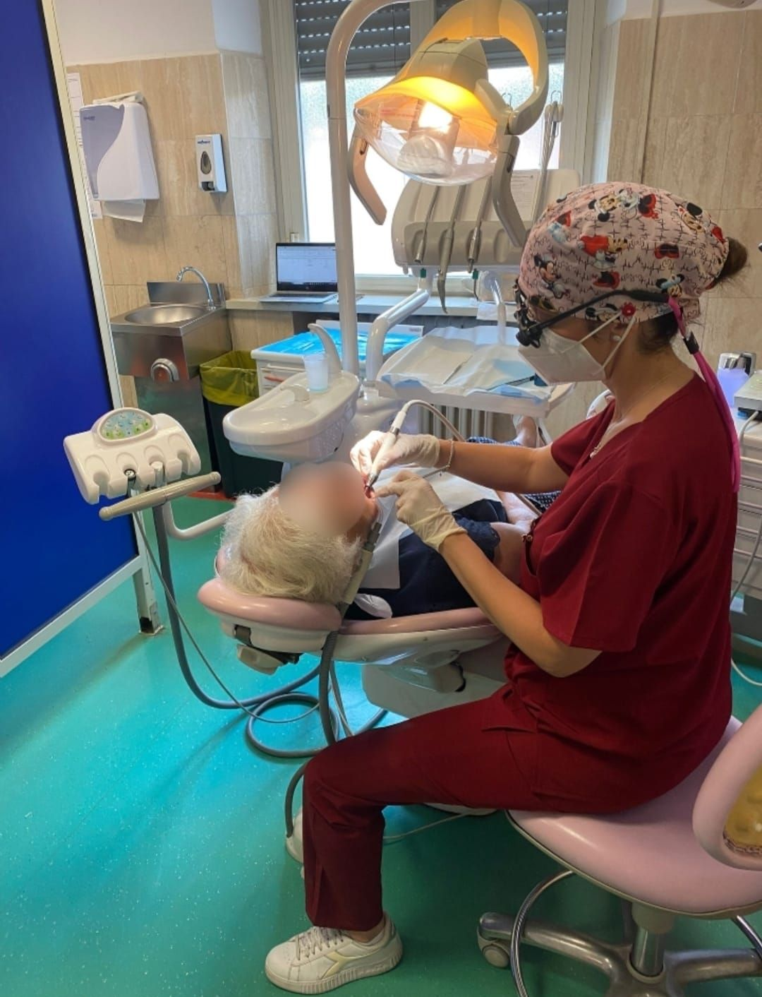 Un dentista in uniforme color bordeaux e berretto decorato esegue una procedura odontoiatrica su un paziente in una clinica.