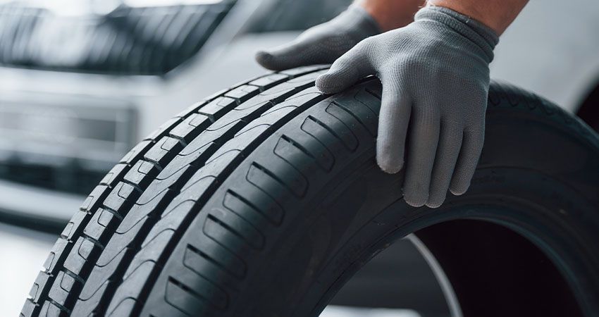 a person wearing gloves is holding a tire in front of a car .