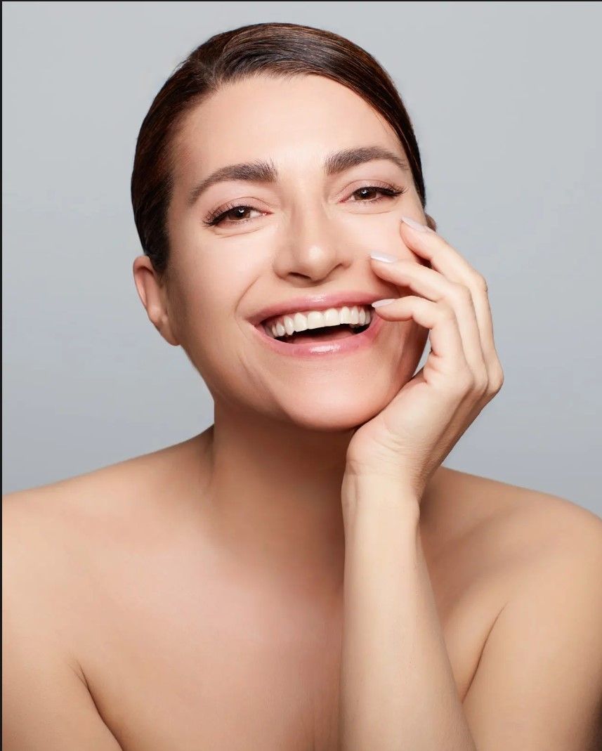 A woman is smiling and touching her face with her hand.
