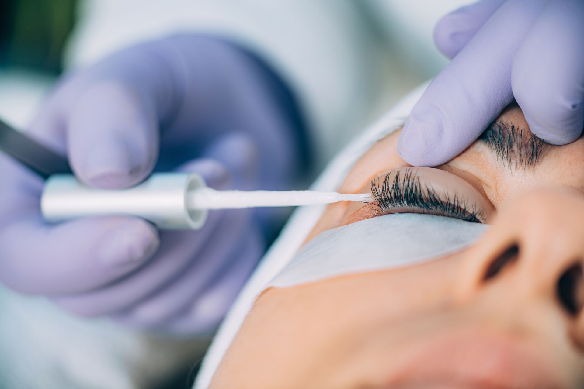 A person in purple gloves applies a lash lifting treatment to a client's eyelashes.