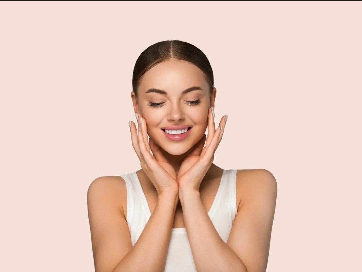 A woman is smiling and touching her face with her hands.