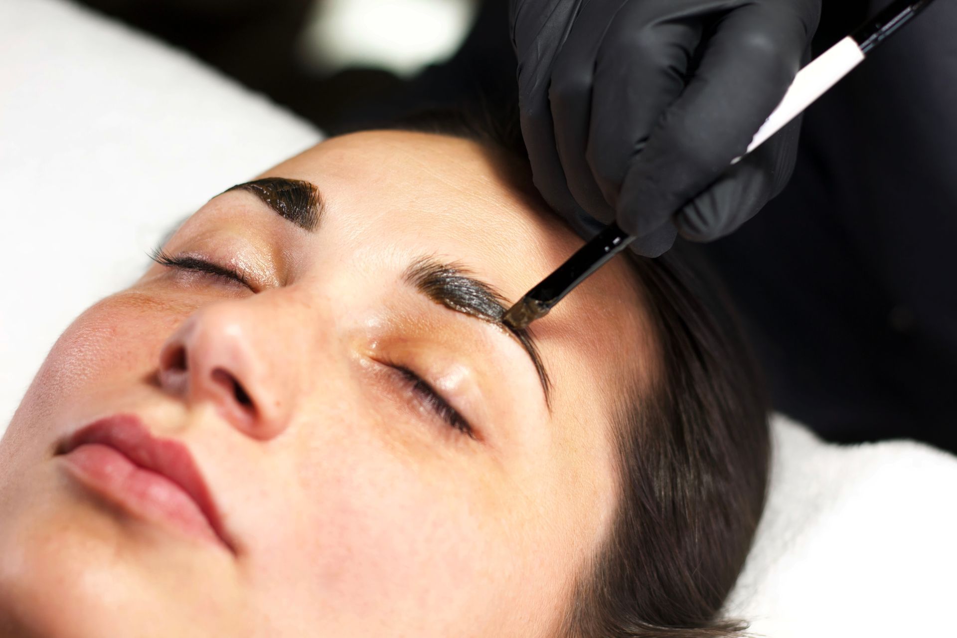 A woman is getting her eyebrows painted with a brush