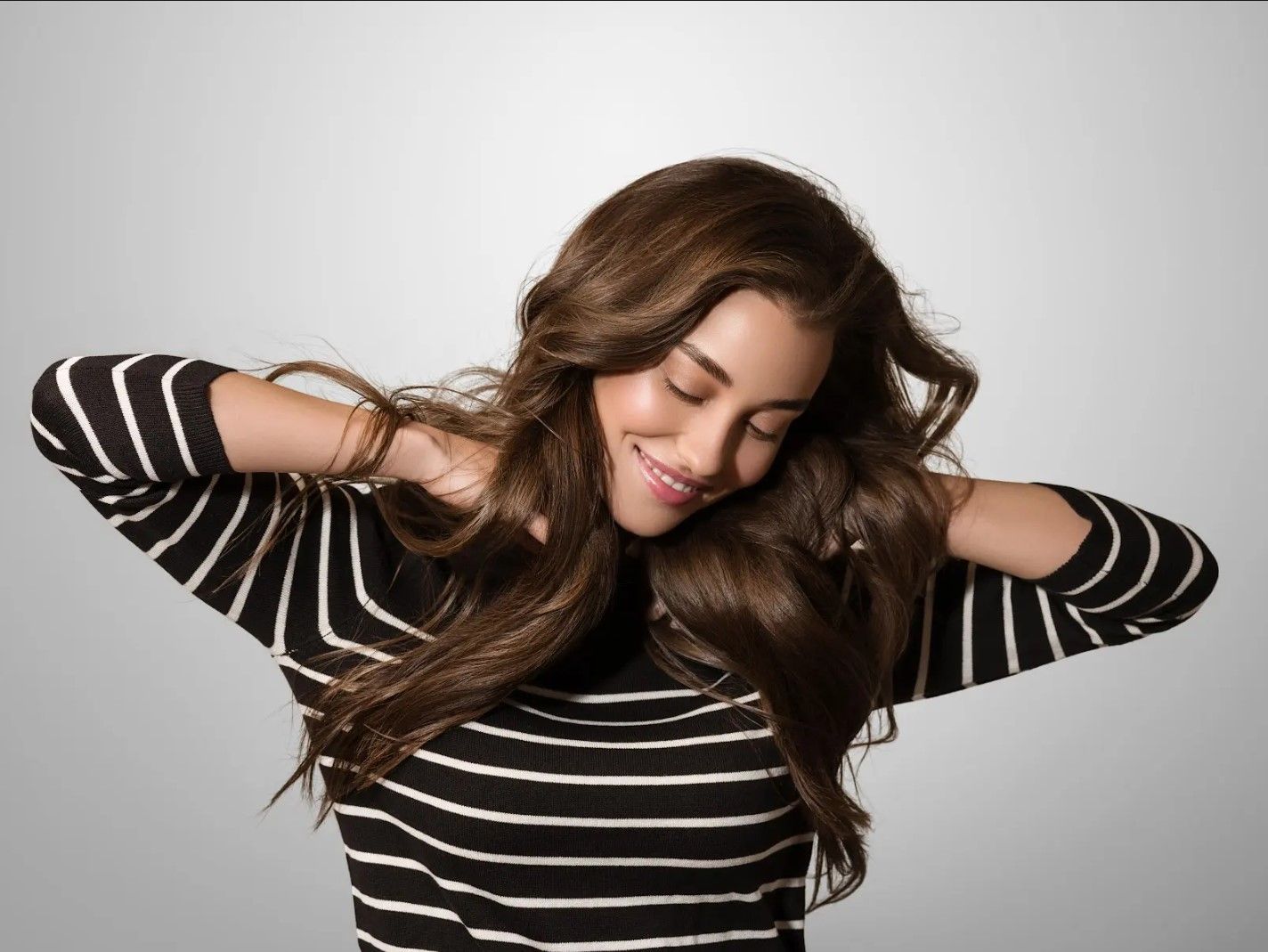 A woman in a black and white striped shirt is smiling with her eyes closed.