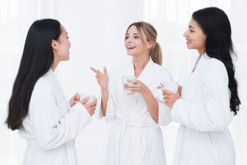 Three women in bathrobes are talking to each other while holding cups of coffee.