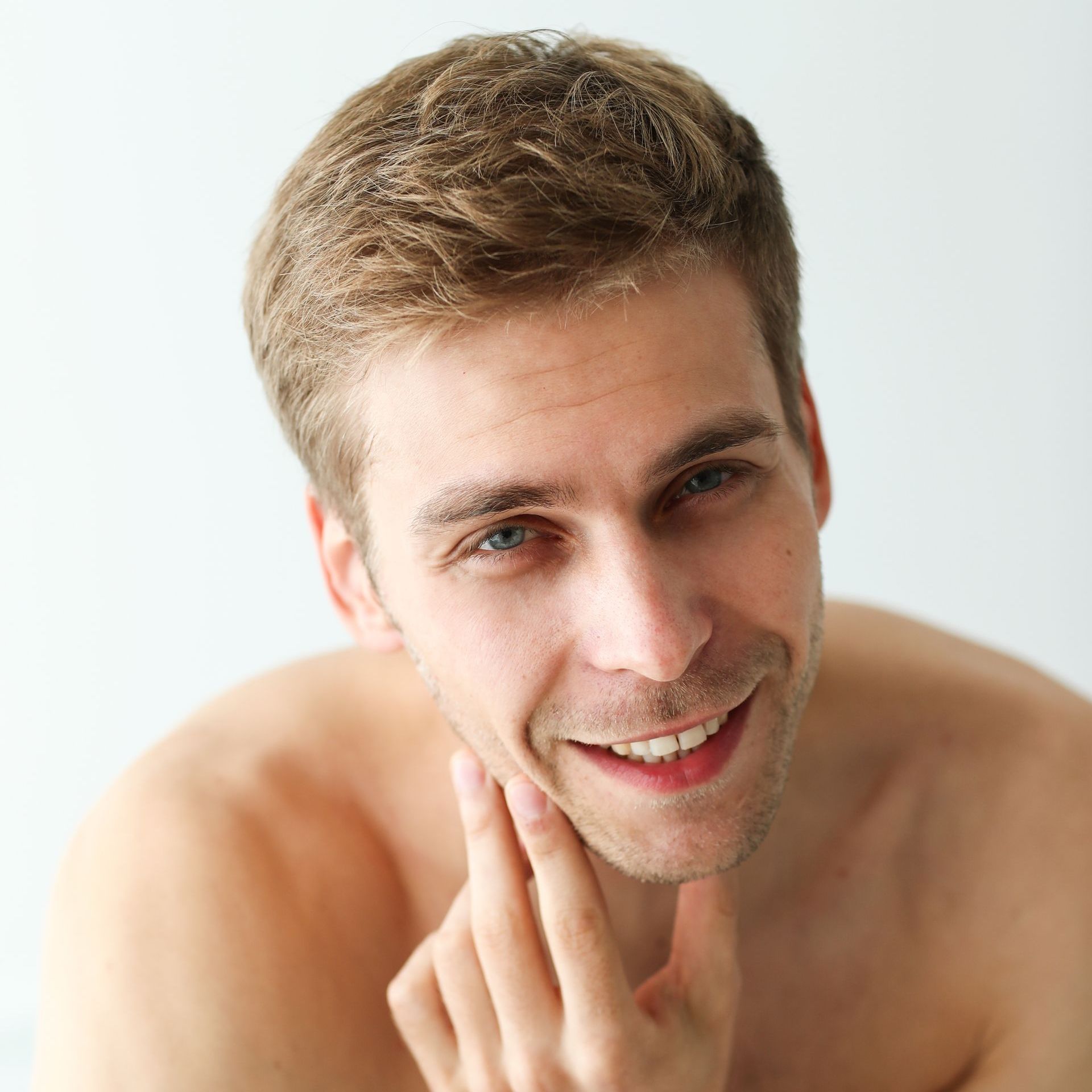 A shirtless man is smiling with his hand on his chin