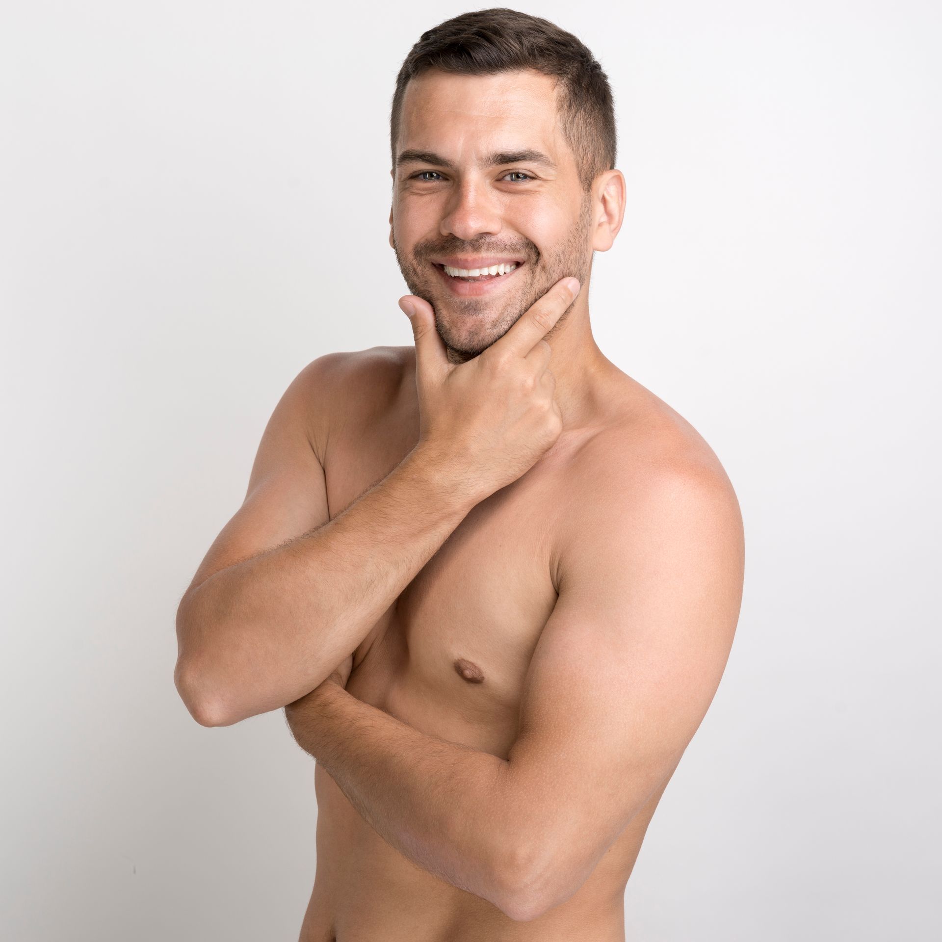 A shirtless man is smiling and holding his hand to his chin.