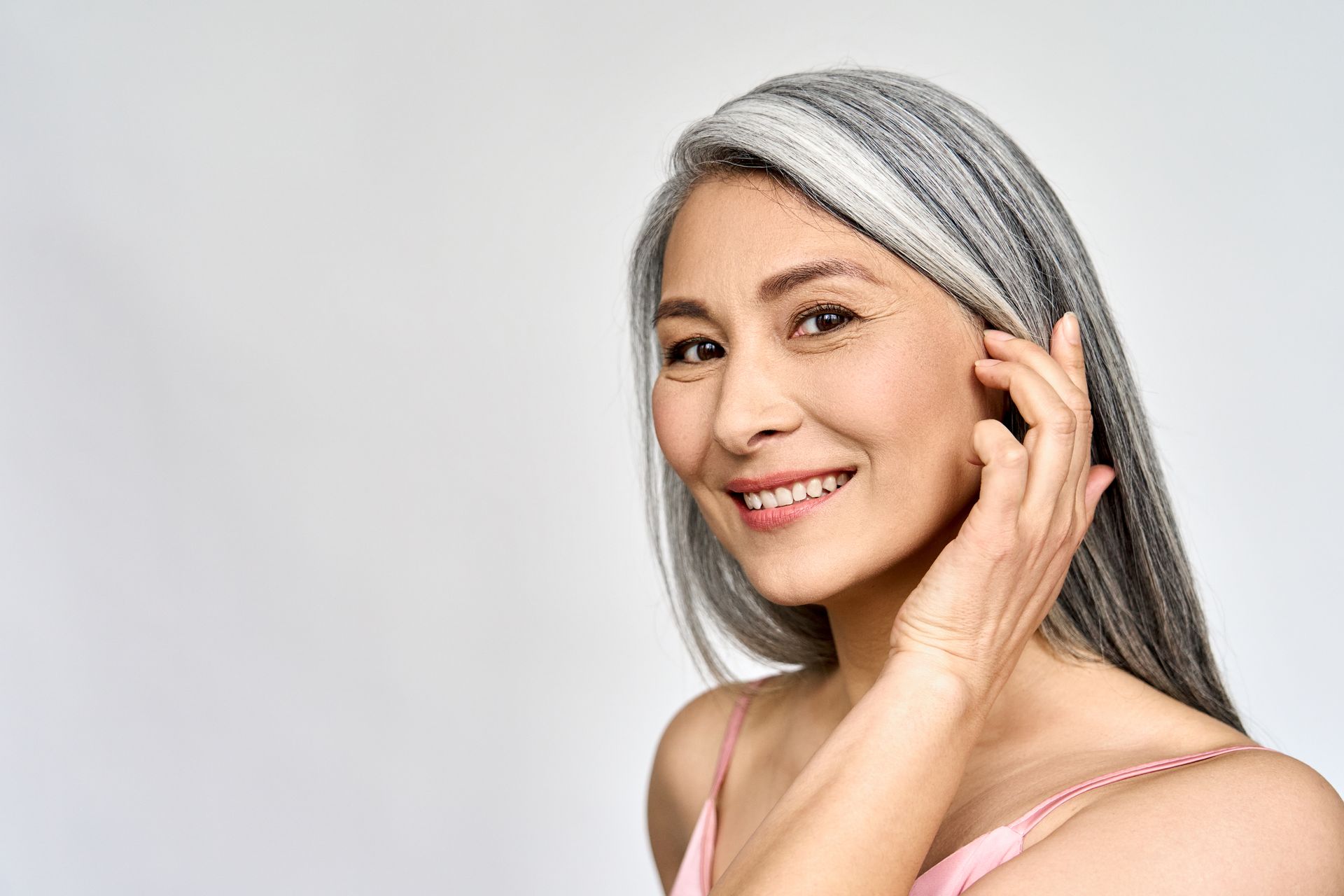 Smiling person with silver hair touching their cheek against a light gray background