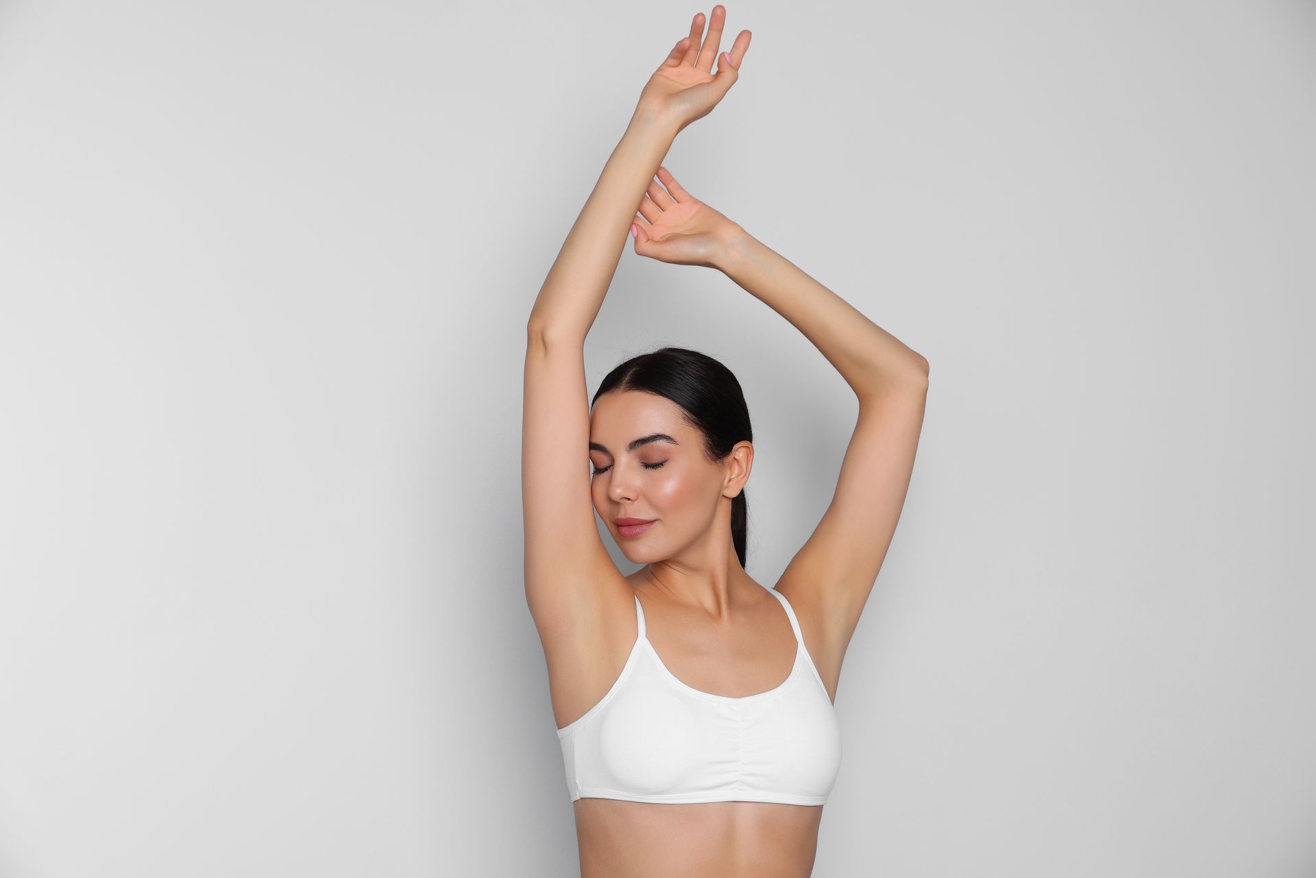 A woman in a white bra is raising her arms in the air.