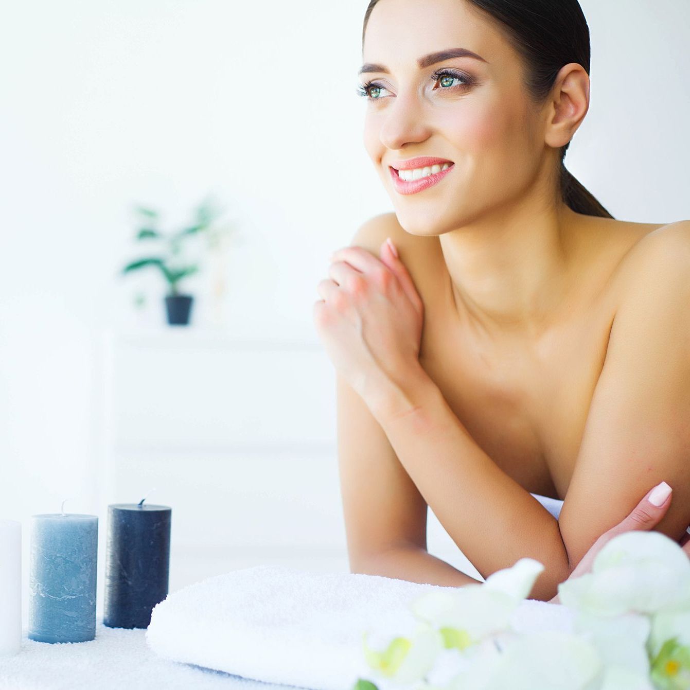 A woman without a shirt is smiling while sitting on a towel