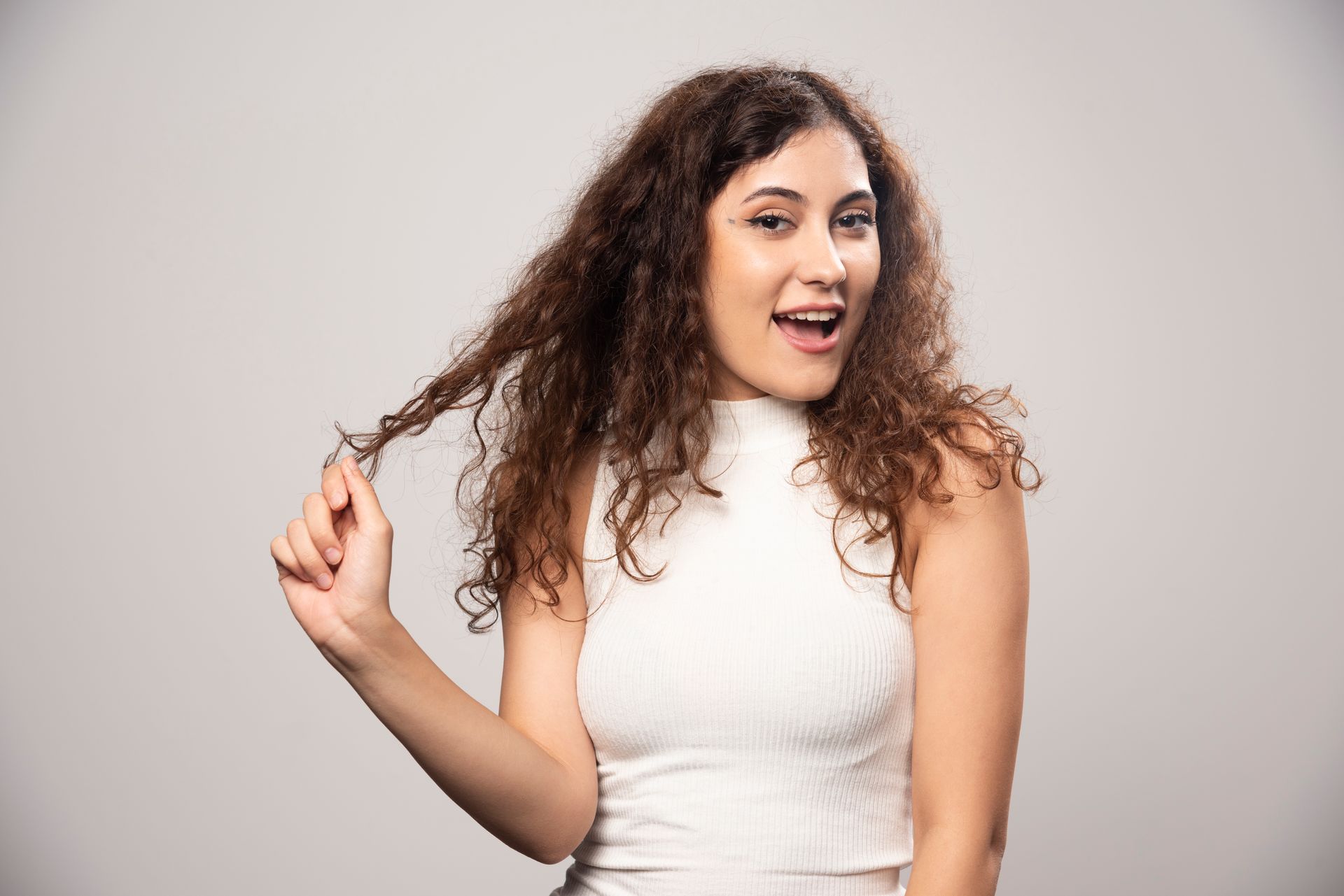 A woman with curly hair is holding her hair in her hand.