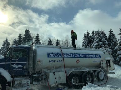 A man is standing on top of a fuel truck in the snow.