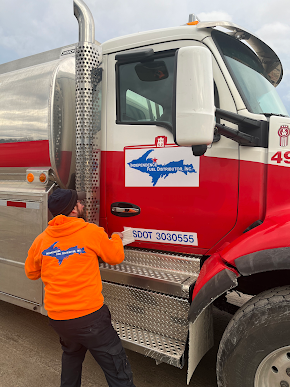 A man in an orange hoodie is standing next to a red and white truck.