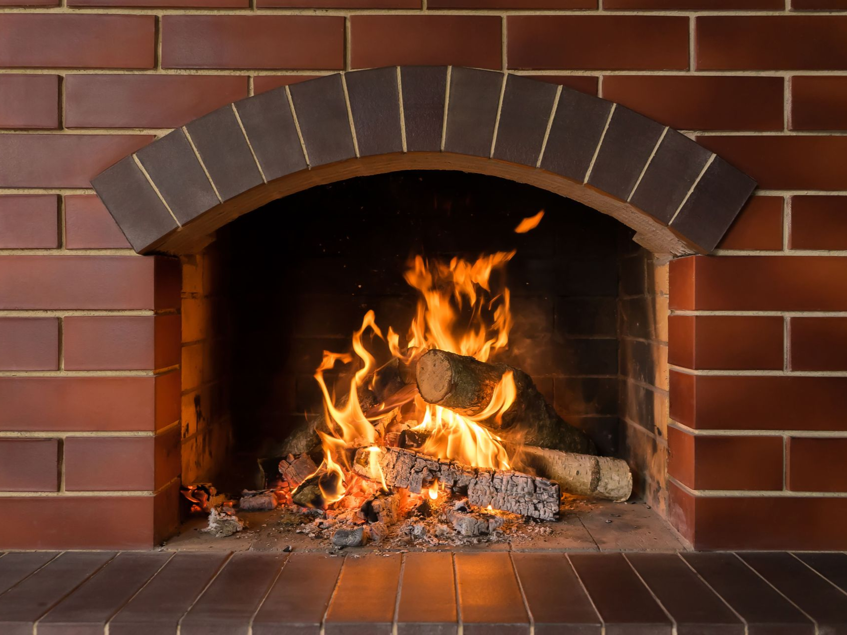 Fireplace with burning logs, flames, red brick surround, and arched top.