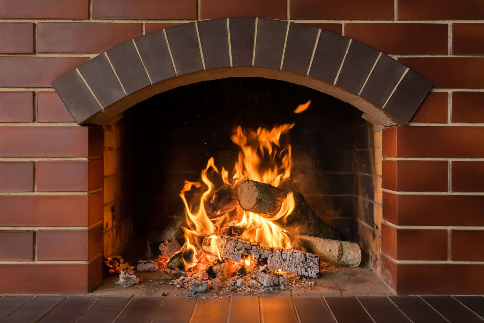 A burning fireplace with flames, wood, and brick arch.