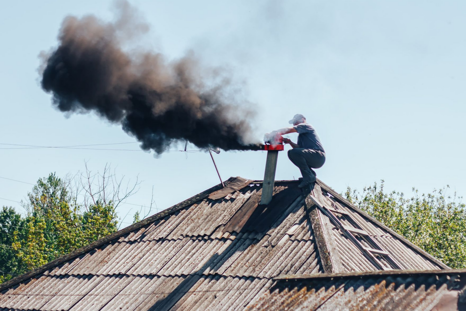 Person on a roof with black smoke billowing from a chimney.