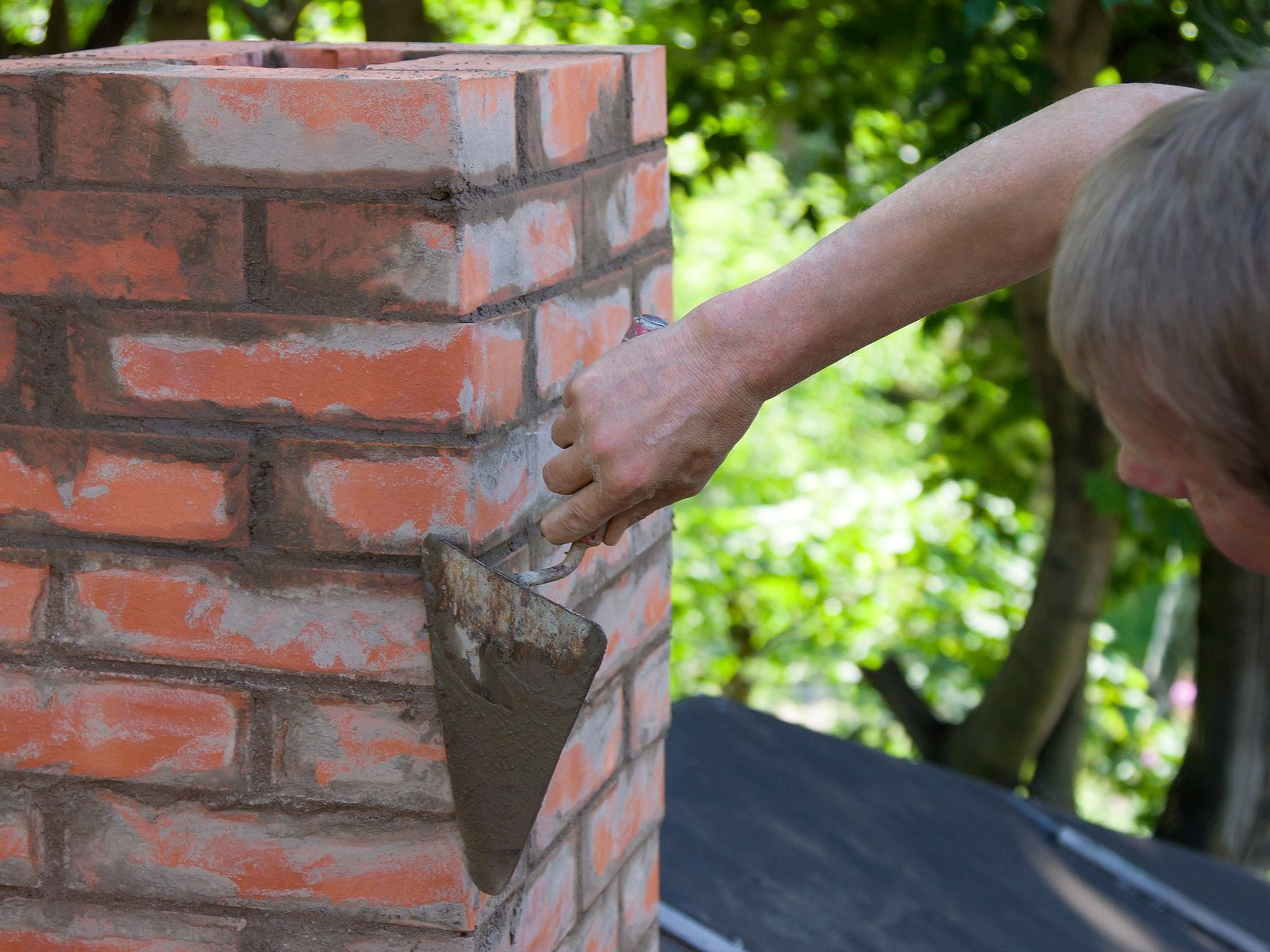 Person using a trowel to apply mortar between red bricks on a chimney.