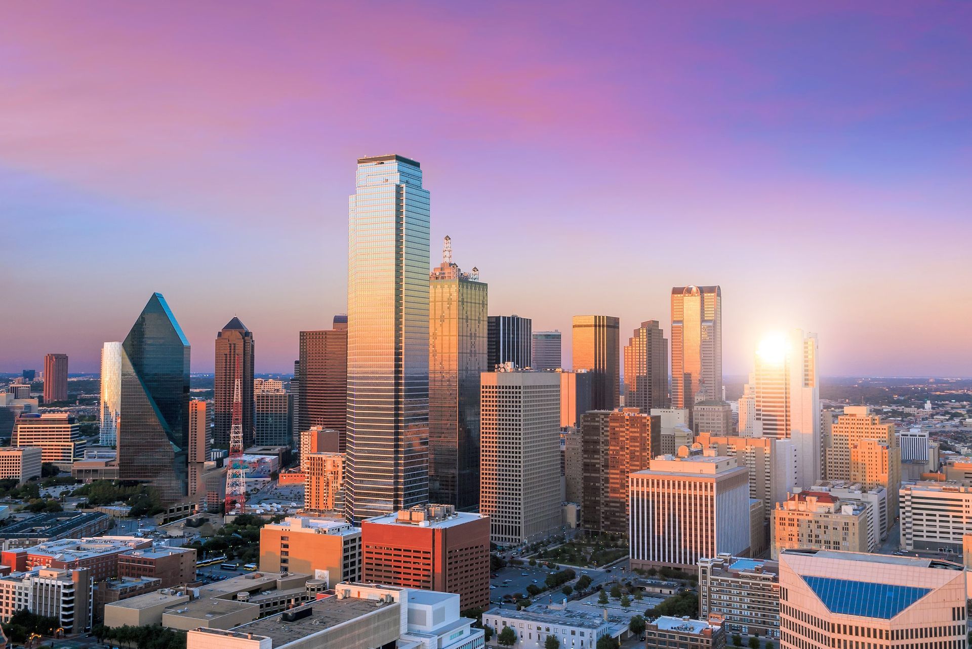 Dallas, Texas skyline at sunset with colorful sky reflecting on buildings.