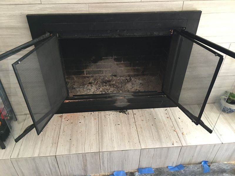 Fireplace with open black doors and screens, sitting on tiled hearth.