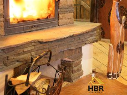 Fireplace with stone facade, flames, wood basket, and a wooden decorative sculpture.
