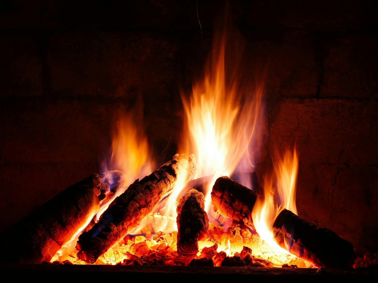 Burning fireplace: flames engulfing logs, emitting orange, yellow, and red light within a dark brick hearth.