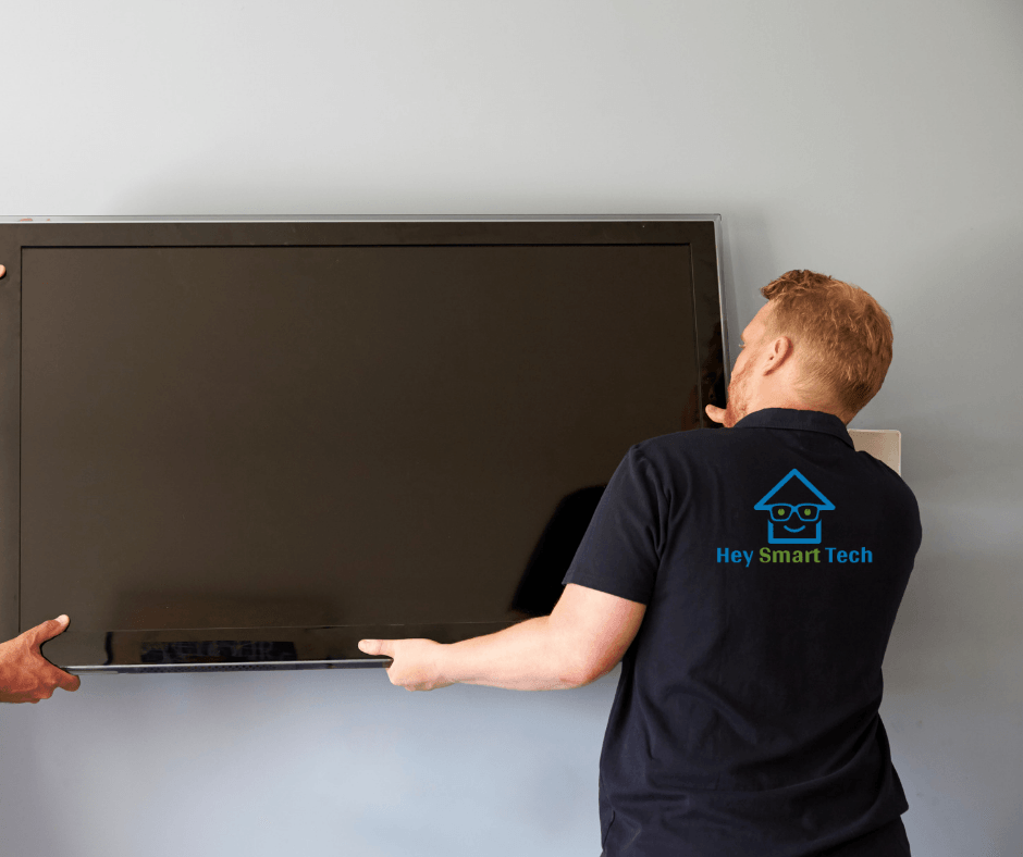Two people mounting a large flat-screen television on a wall. One is wearing a black shirt with a company logo.