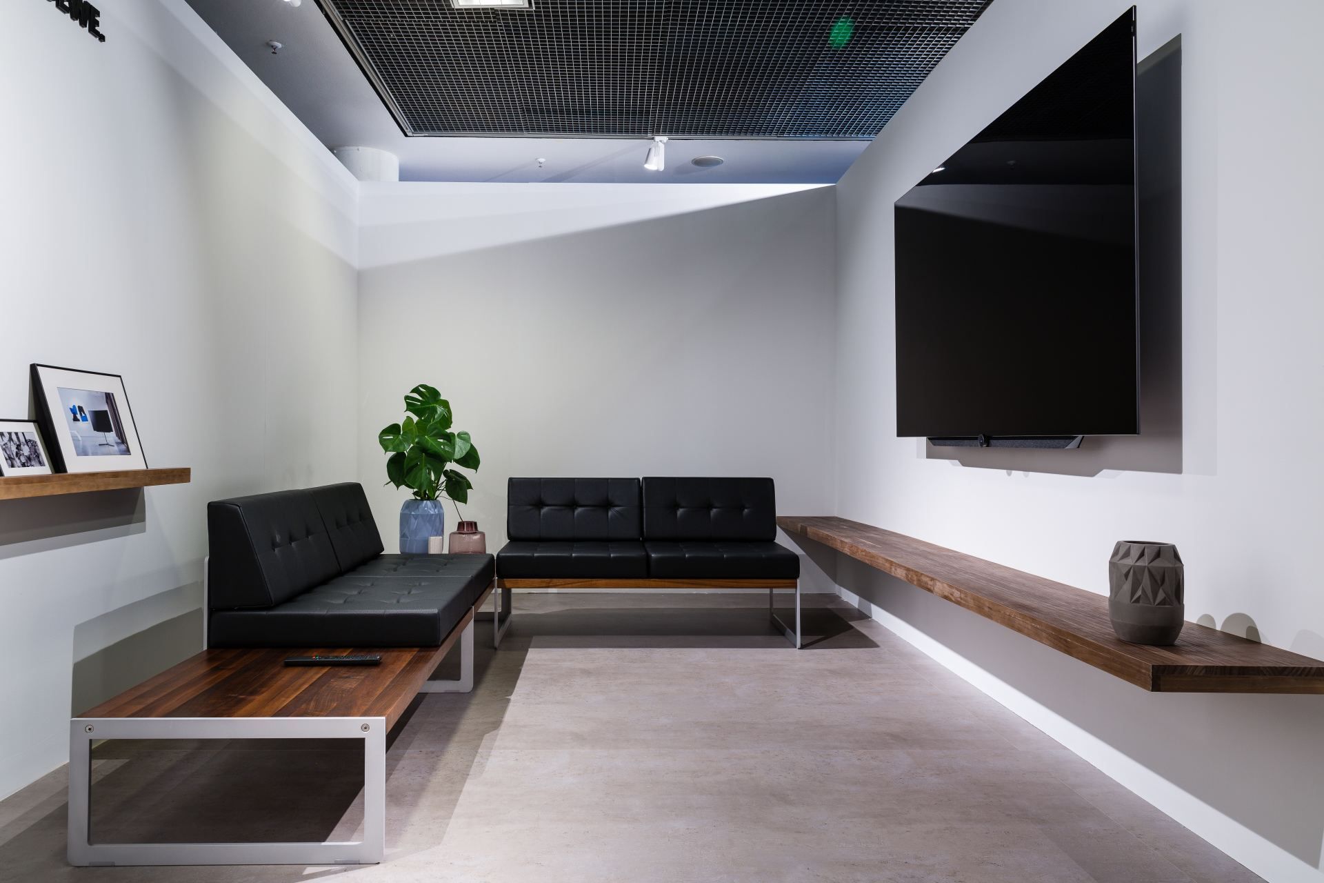 Modern minimalist lounge with black leather sofas, floating shelves, and large TV.