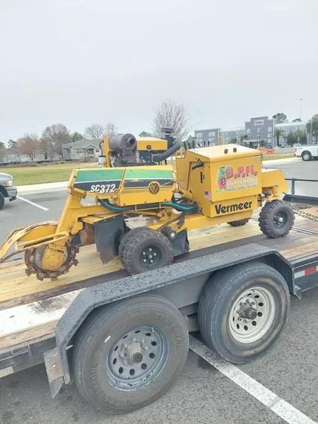 A yellow Vermeer stump grinder secured on a flatbed trailer in a parking lot.