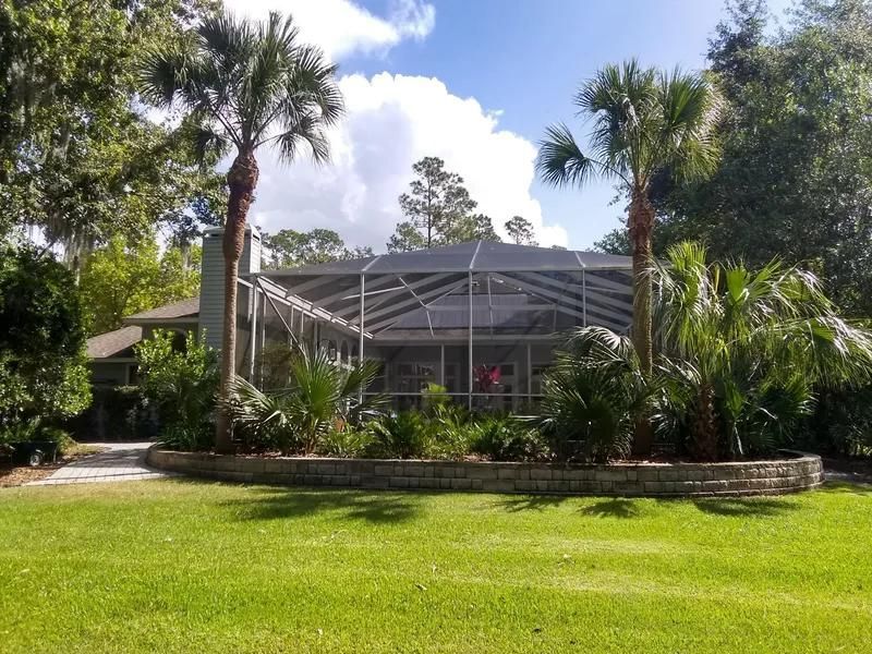 A house with a large, screened-in patio, surrounded by lush green trees, palm trees, and a manicured lawn.
